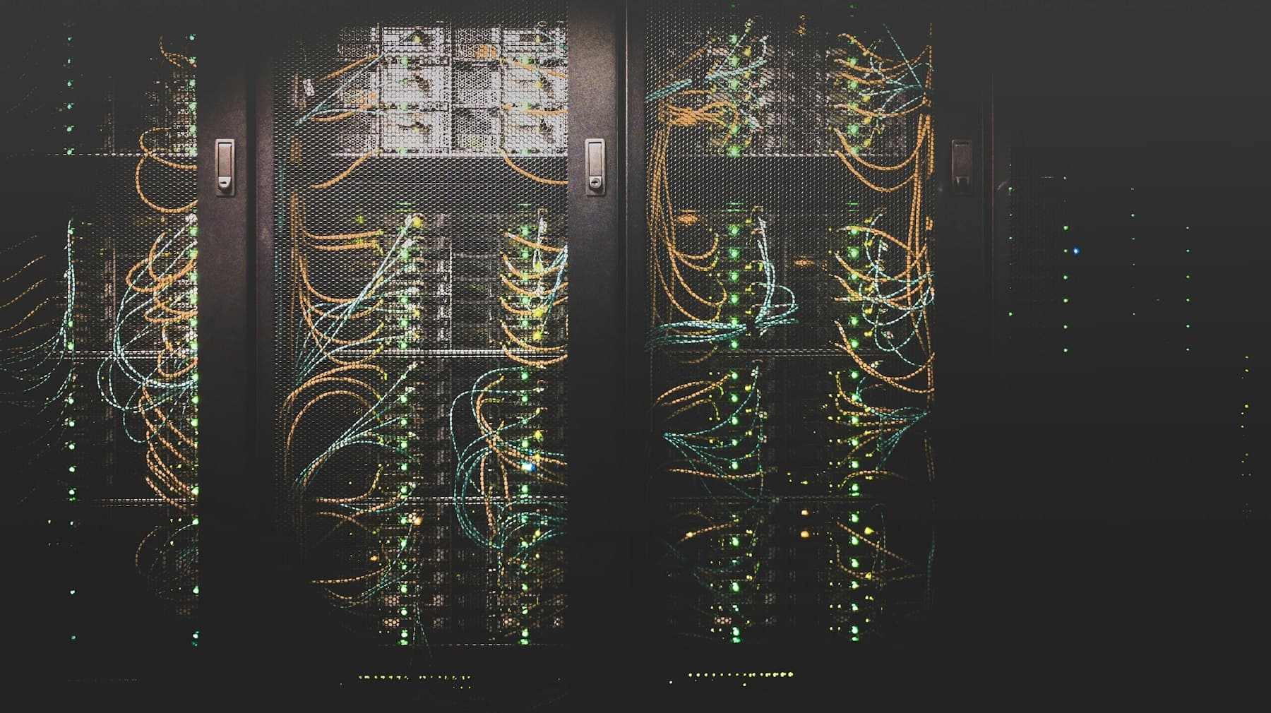 Server racks in a dark data center with green status lights and colored cables