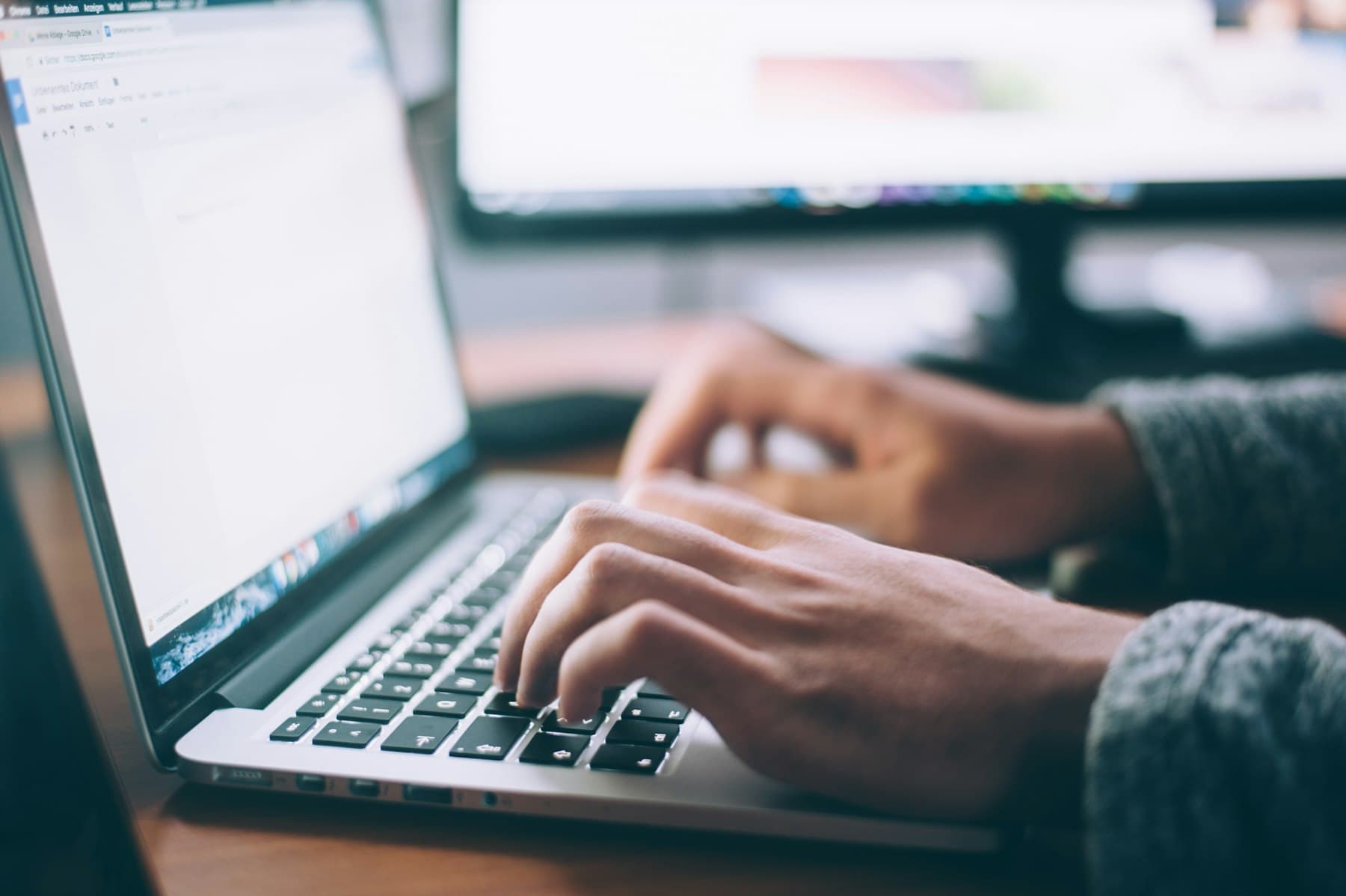 Hands typing on a silver laptop on a wooden desk